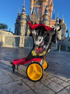 A red Mickey Mouse-themed Disney rental stroller parked in front of Cinderella Castle